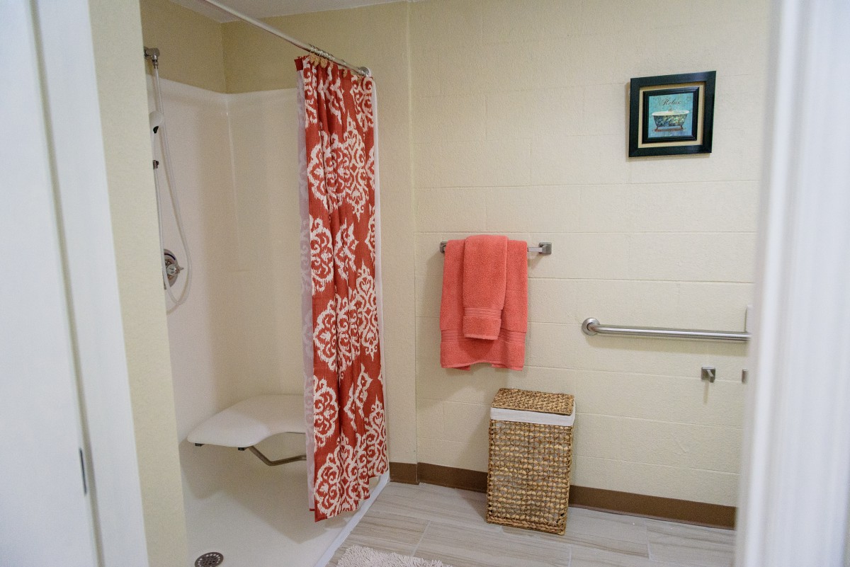A bathroom featuring a shower with a patterned curtain, an orange towel hanging on a rail, and a wicker basket.