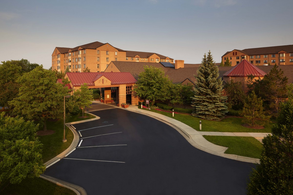 A hotel building with a driveway and surrounding greenery.