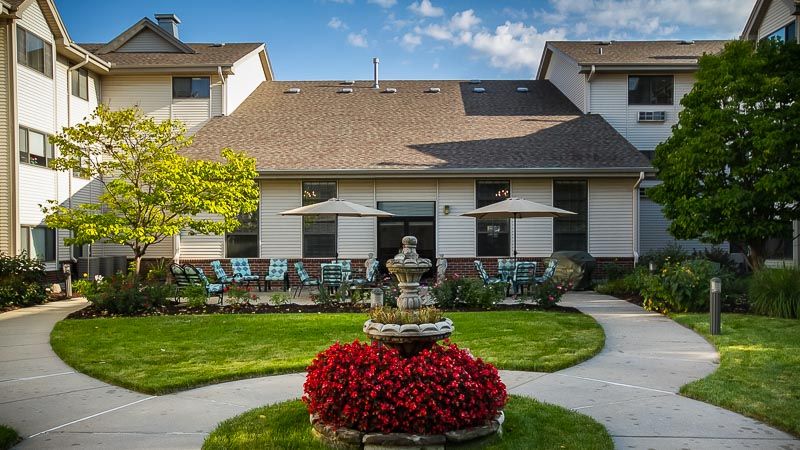 A beautiful outdoor area with a fountain surrounded by vibrant flowers and a well-maintained garden in front of a residential building.
