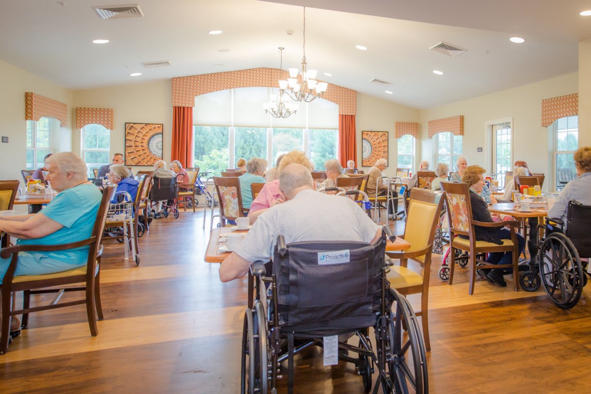 Elderly residents gather in a nursing home dining hall.
