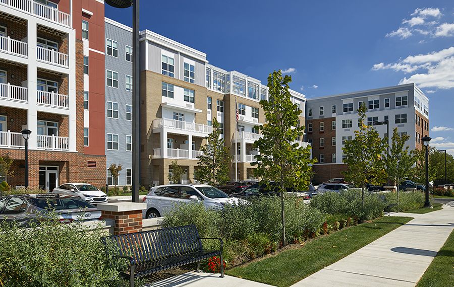 A modern apartment complex in an urban residential area with well-maintained landscaping and parked cars.