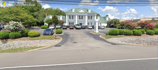 A view of a hotel with a spacious parking lot surrounded by greenery.