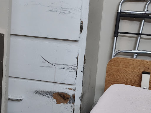 A close-up view of a damaged white wooden cabinet with visible scratches and wear.