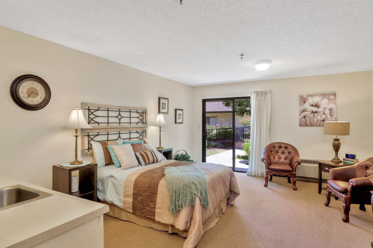 A cozy bedroom with a neatly made bed, stylish lamps, and a large window providing natural light.