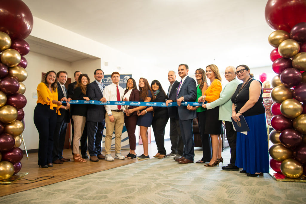 A group of people gathered for a ribbon-cutting ceremony indoors.