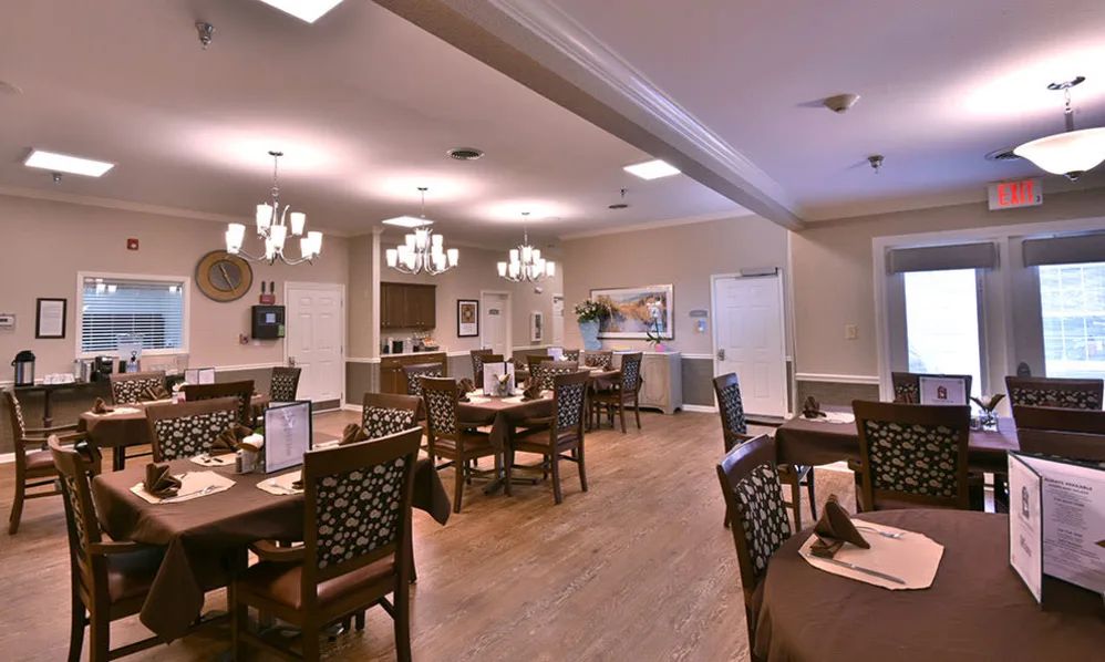 A cozy dining room with neatly arranged tables and chairs, illuminated by elegant chandeliers.