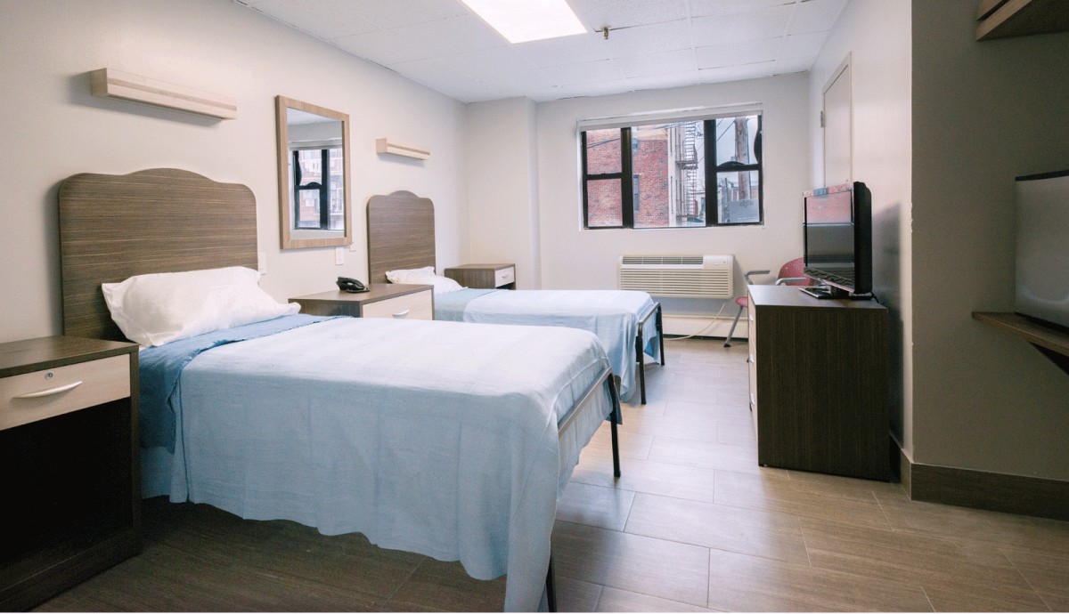A clean hospital room with two patient beds and windows providing natural light.