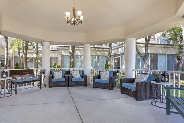 A spacious outdoor patio with wicker furniture and cushioned seating under a gazebo, featuring a chandelier and surrounded by columns.
