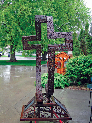 A striking metallic cross sculpture set in a serene garden.
