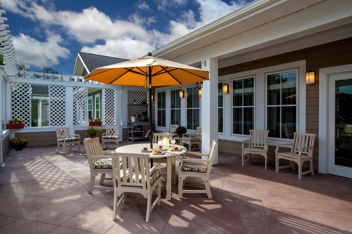 A sunny outdoor patio with a table and chairs under a large umbrella.