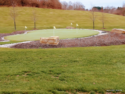 A serene putting green surrounded by grass and gentle hills.