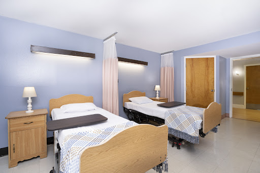 A view of a hospital patient room featuring two beds with bedside tables and curtains for privacy.