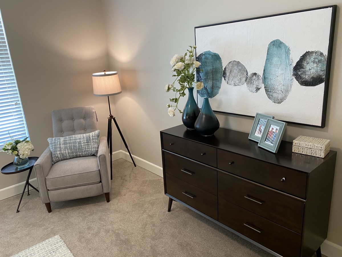 A cozy living room corner with an armchair, floor lamp, and decorative elements on a dresser.