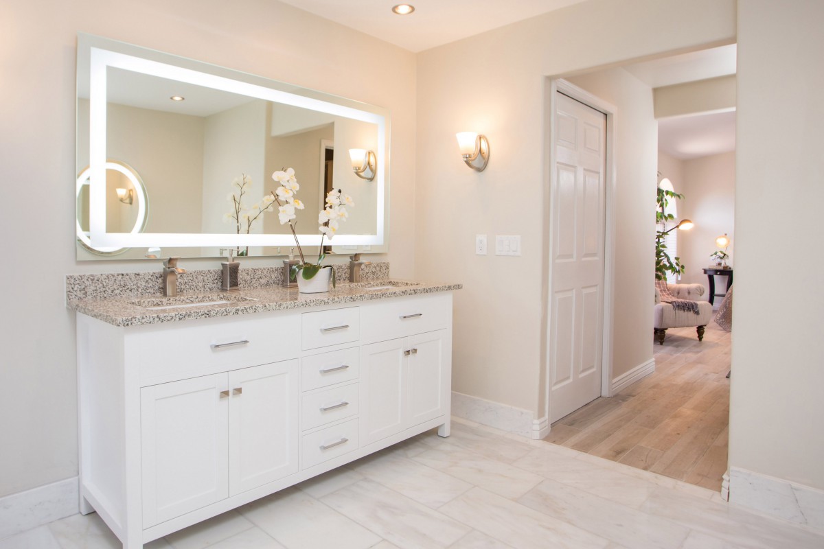 A modern bathroom with a large illuminated mirror and sleek white cabinetry.
