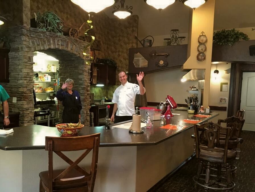 A chef waves in a cozy kitchen setting.