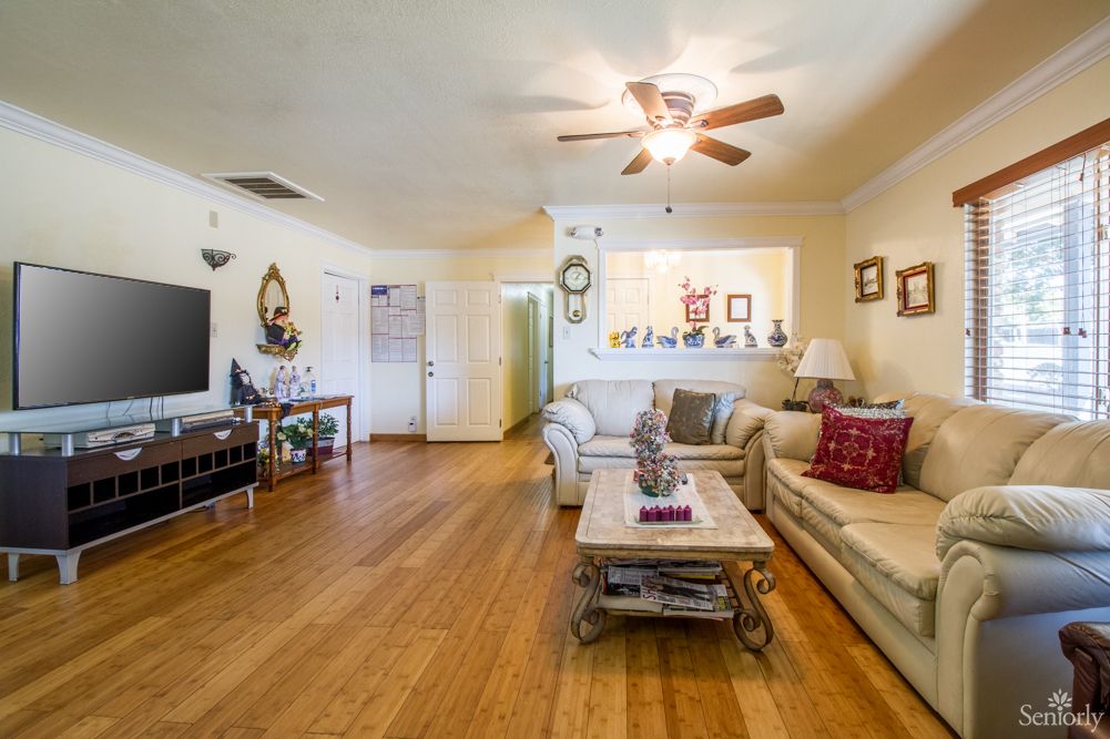 A cozy living room with wooden floors, featuring comfortable sofas, a coffee table, a ceiling fan, and a television.