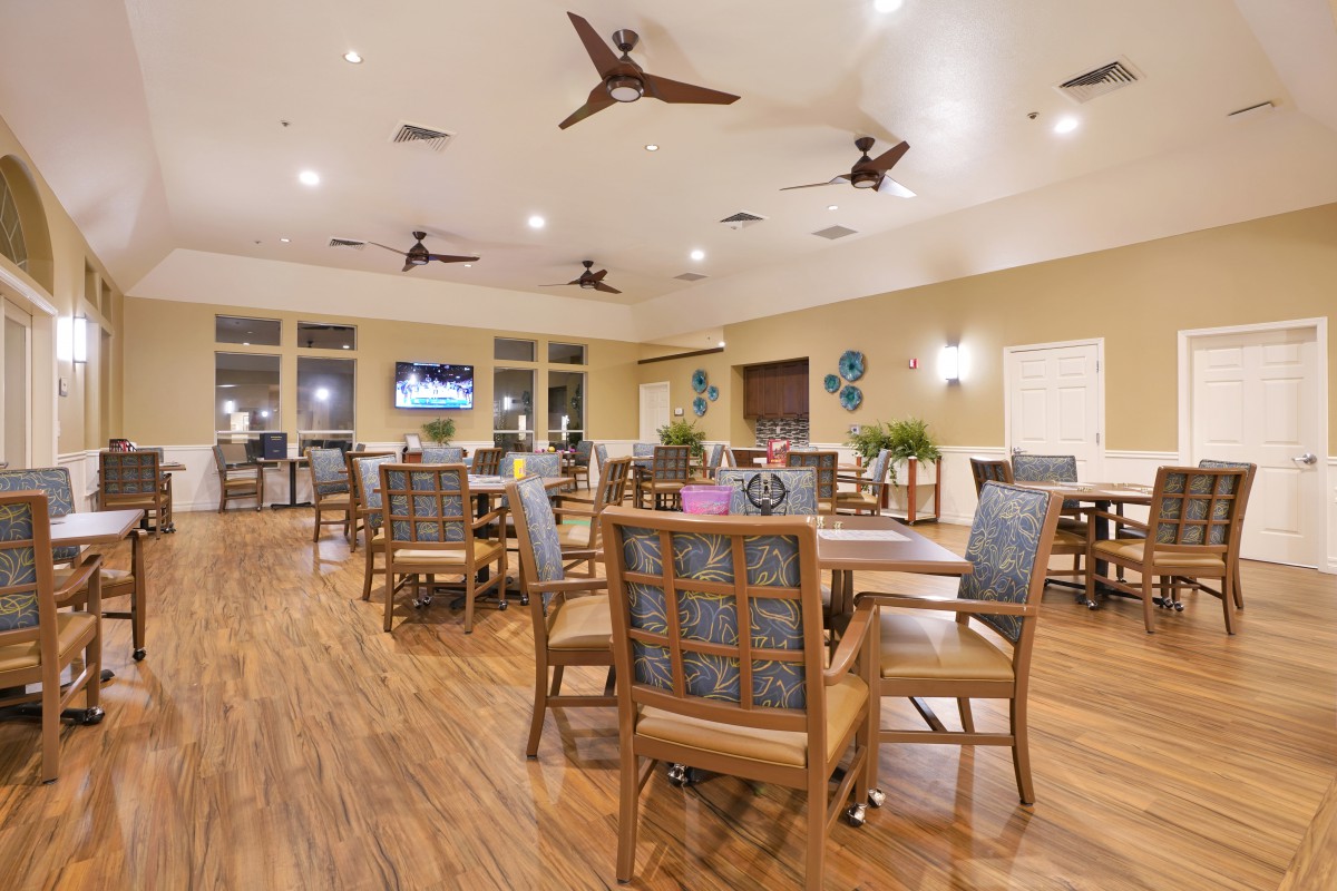 A spacious indoor dining area with wooden floors, neatly arranged tables and chairs, and ceiling fans.