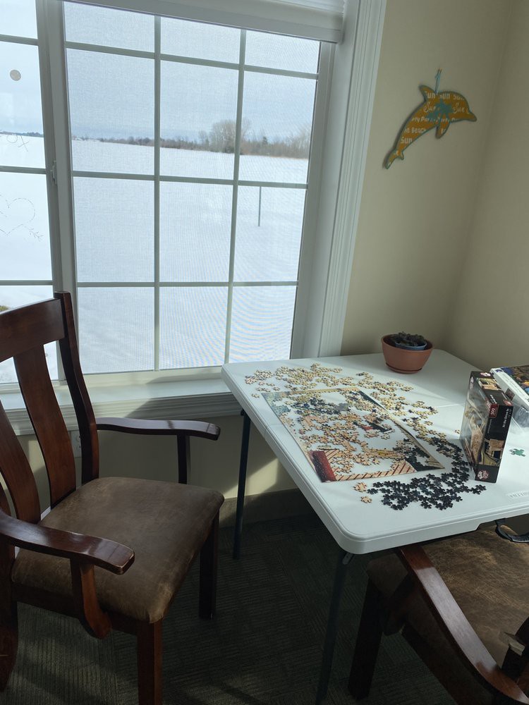 A cozy indoor setting with a puzzle spread out on a table near a window showing a snowy landscape outside.