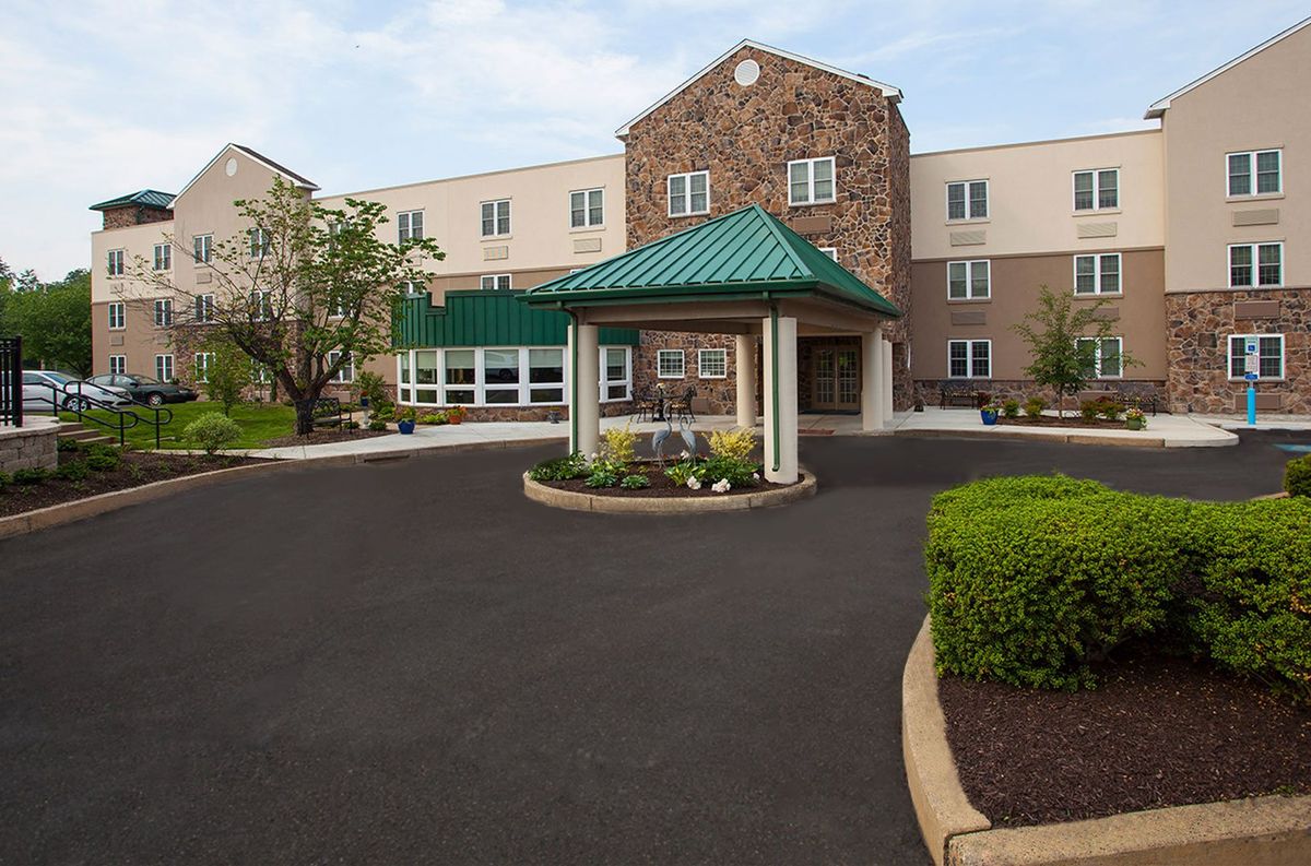 A view of a building entrance with a canopy over the driveway, surrounded by landscaped gardens.