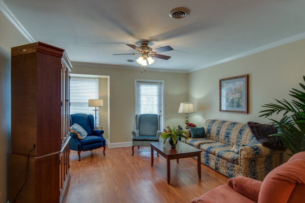 A cozy living room with a sofa, chairs, coffee table, ceiling fan, and wooden flooring.