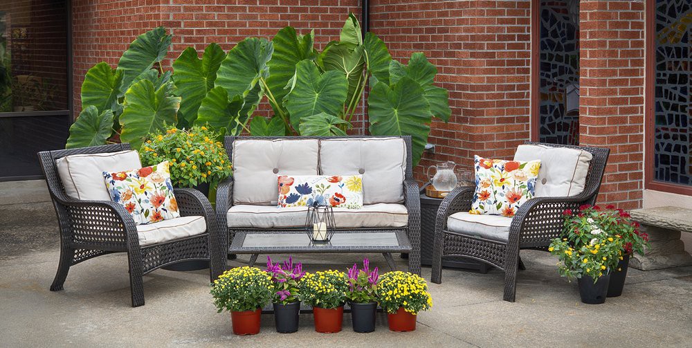 A cozy outdoor patio setup with a sofa, chairs, colorful cushions, and potted plants against a brick wall.