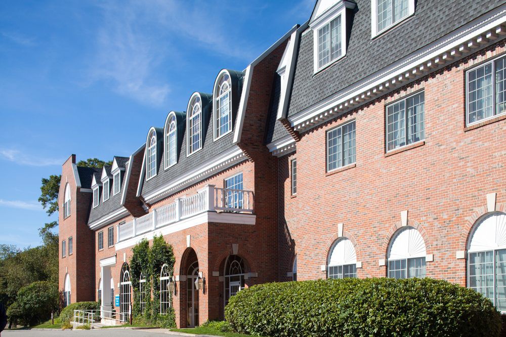 A row of brick buildings with arched windows and a sloped roof under a clear blue sky.