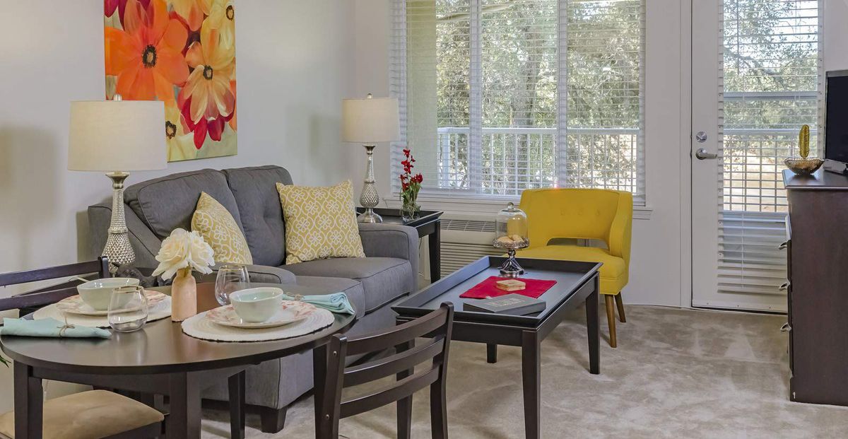 A cozy living room with a gray sofa, a yellow chair, and a coffee table near a large window.