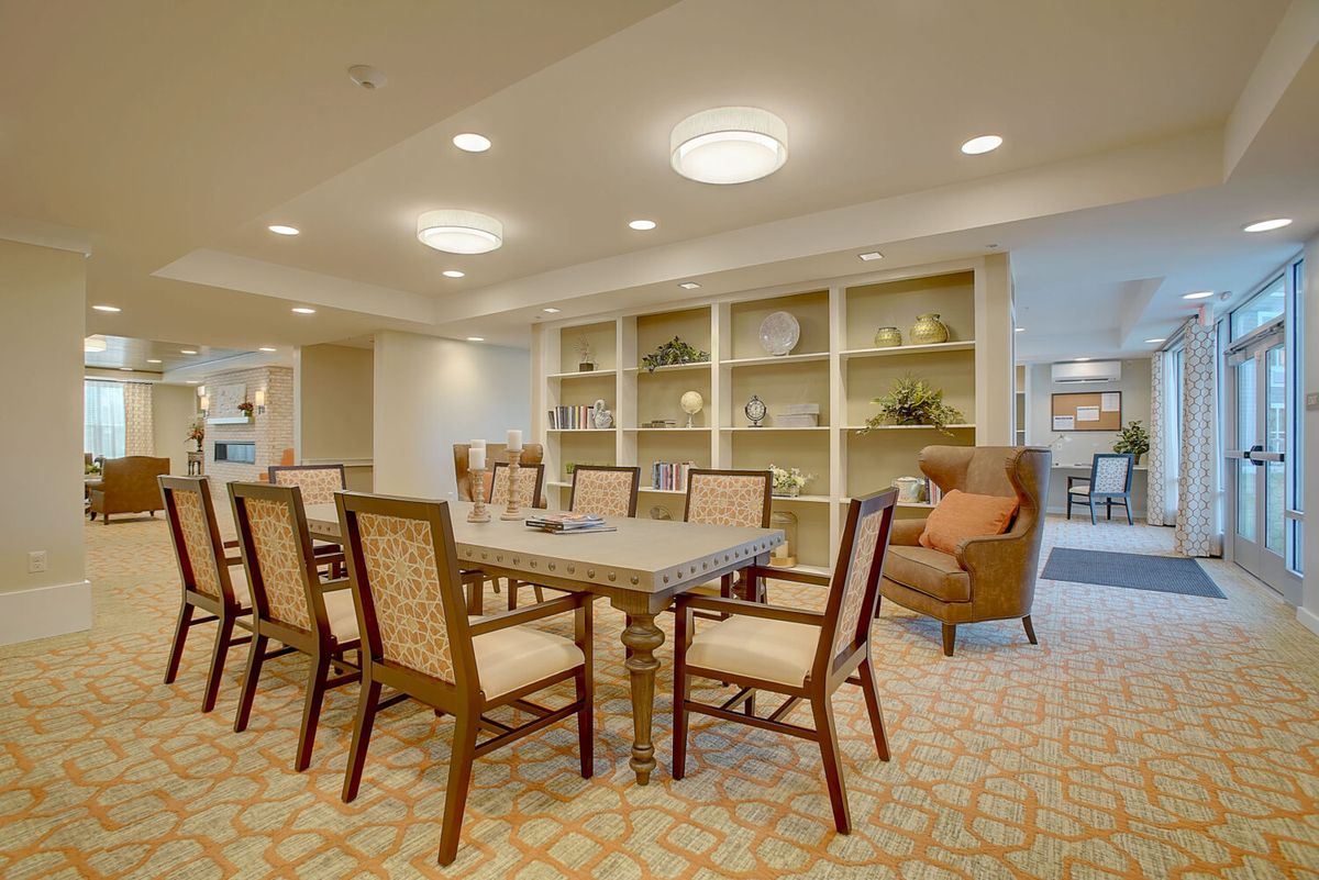 A well-lit dining area featuring a large table, multiple chairs, and a bookshelf in the background.