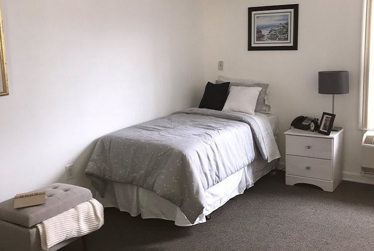 A minimalist bedroom featuring a single bed with gray bedding and a nightstand.