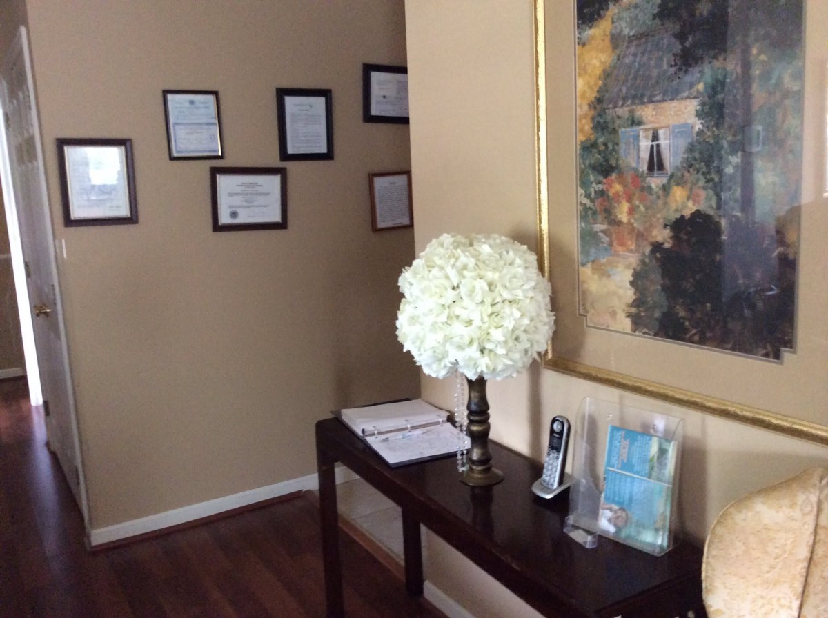 A hallway with a decorative table, flowers, and framed certificates on the wall.