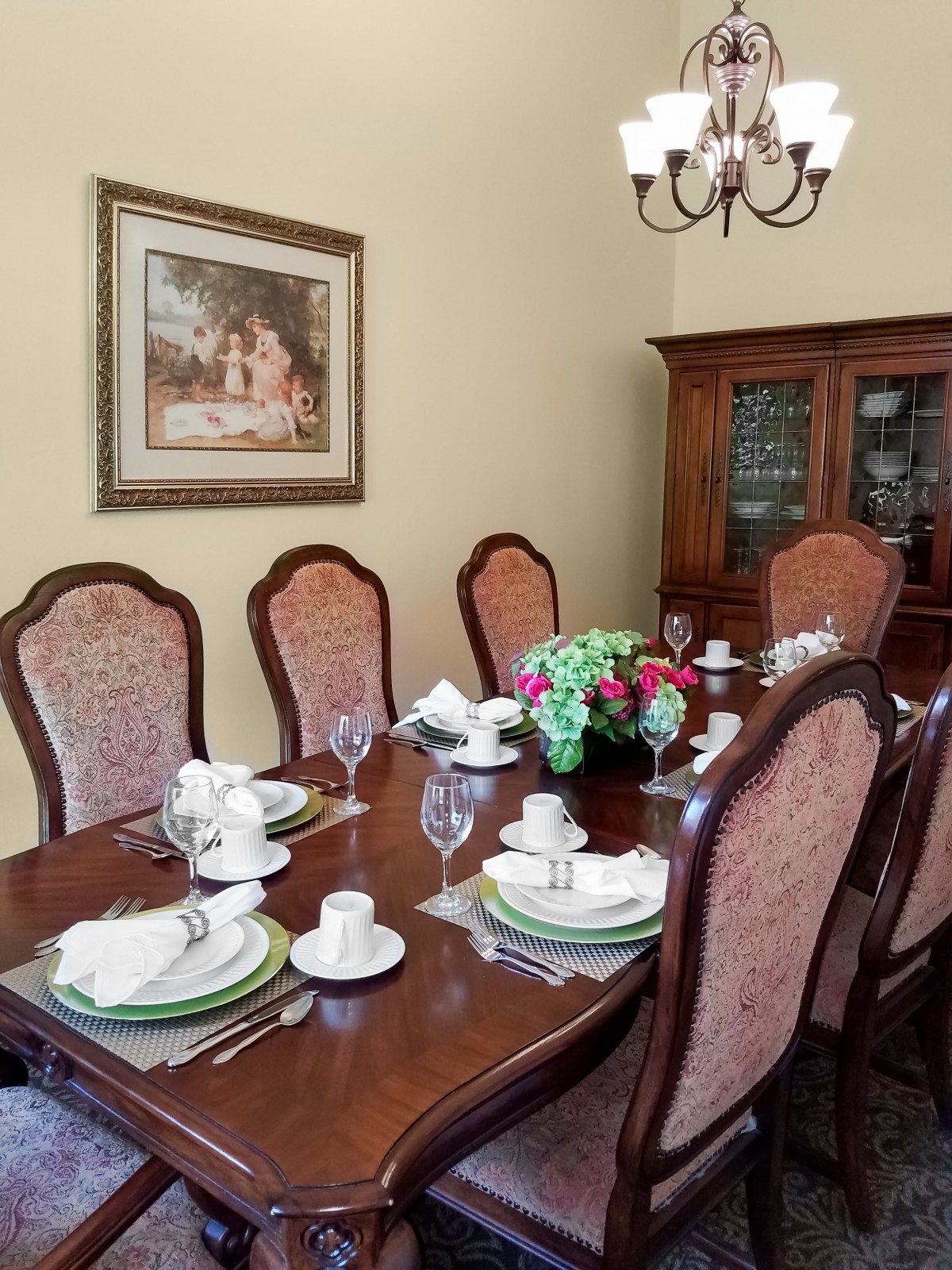 A dining room with a neatly set table, surrounded by upholstered chairs and adorned with a floral centerpiece.