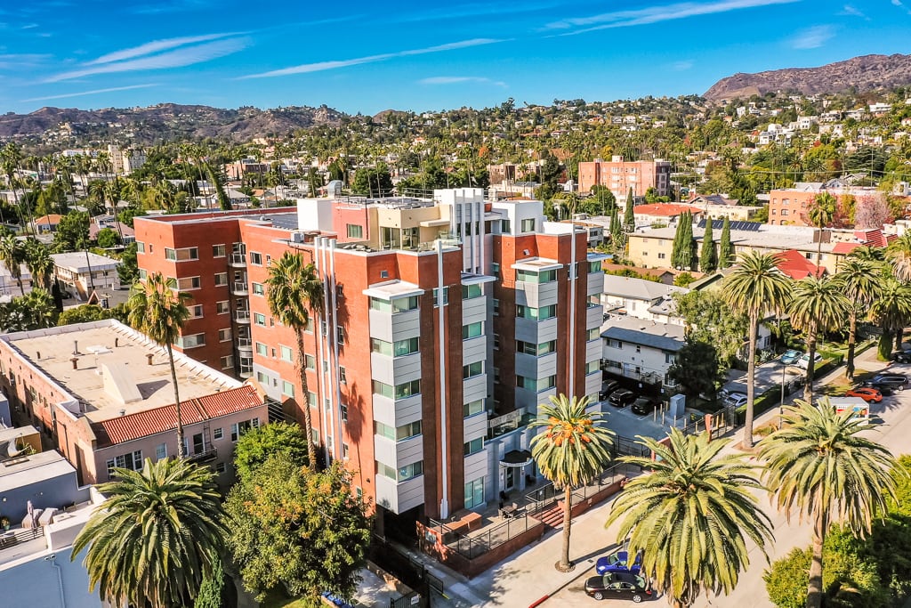 Aerial view of a residential building surrounded by palm trees in an urban setting.