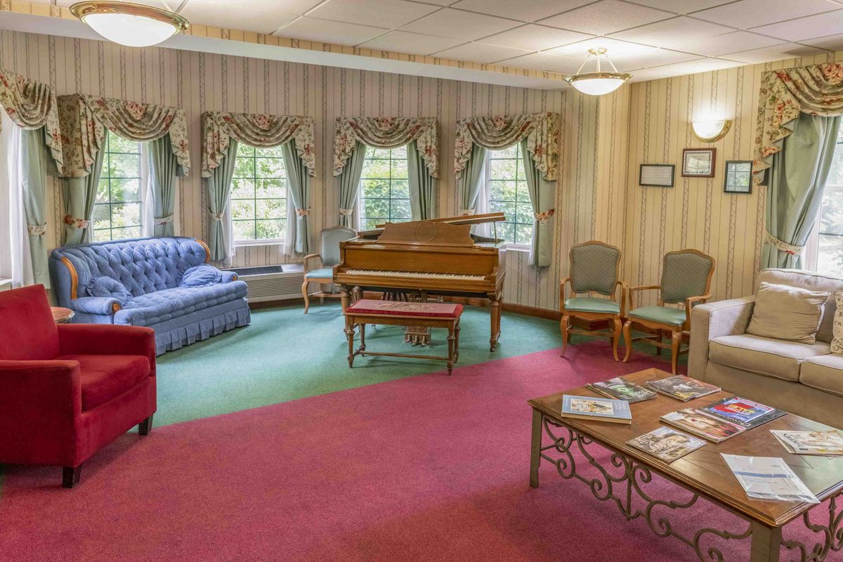 A cozy living room with a piano, seating area, and large windows.