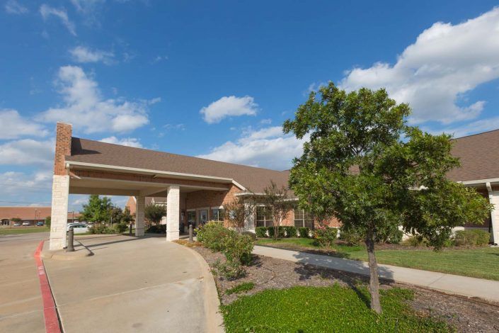 A healthcare facility with a spacious entrance and landscaped surroundings under a bright blue sky.