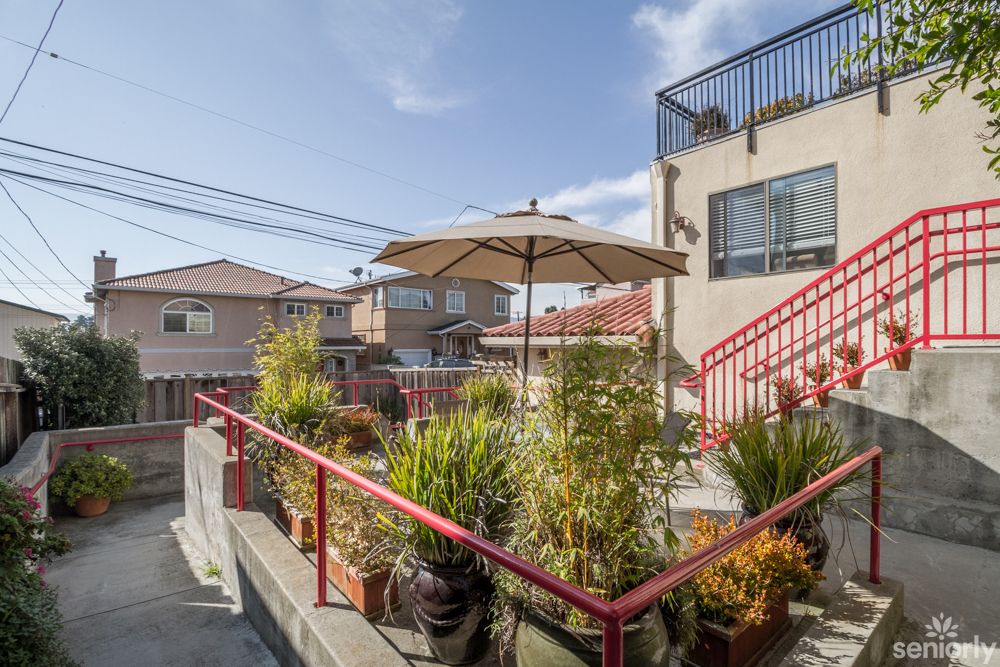 An outdoor patio with potted plants and an umbrella, adjacent to a building in an urban setting.