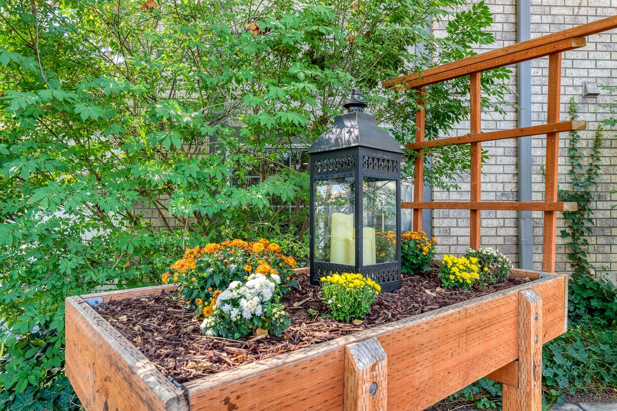 A decorative lantern surrounded by vibrant flowers in a raised wooden planter box.