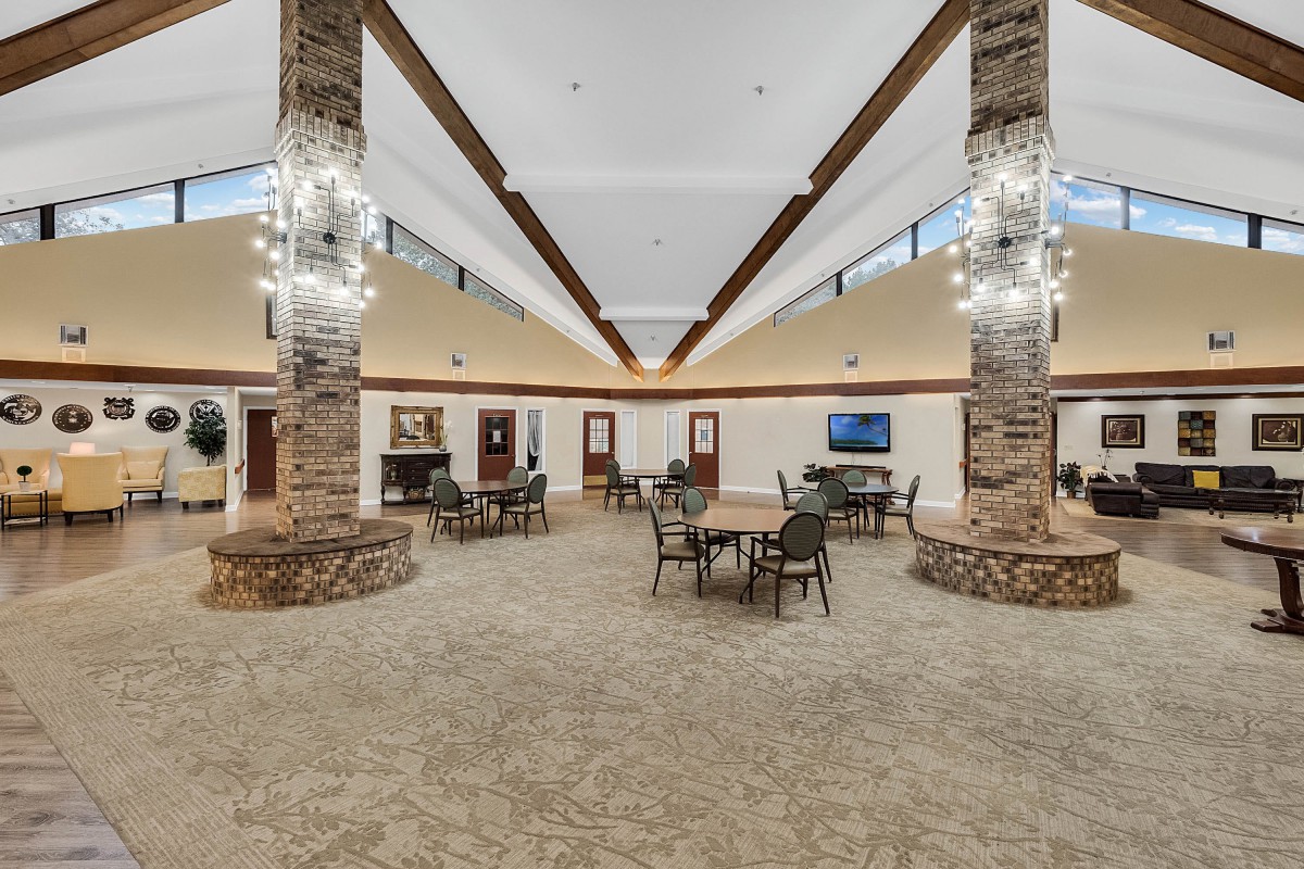 A spacious lounge area with stone pillars, chandeliers, and tables and chairs arranged on a carpeted floor.