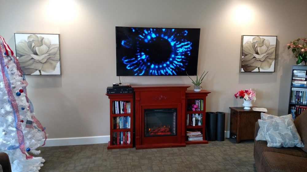 A cozy living room setup features a wall-mounted television above a fireplace with books and decor on the shelves.