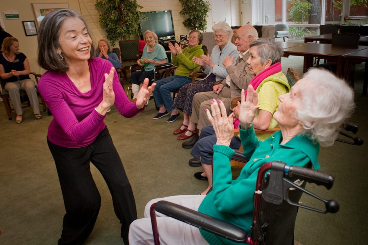 A group of elderly individuals participating in a lively exercise session led by an instructor indoors.