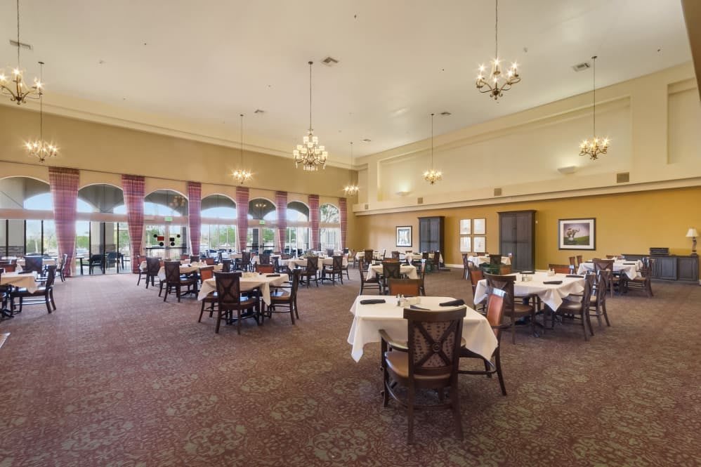 An elegant restaurant dining room with neatly arranged tables and chairs, illuminated by chandeliers.