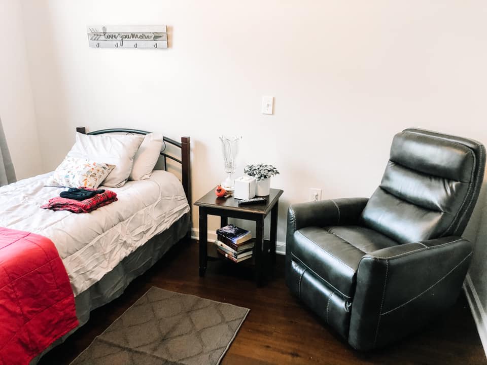 A cozy bedroom featuring a neatly made bed, a comfortable armchair, and a side table with books.