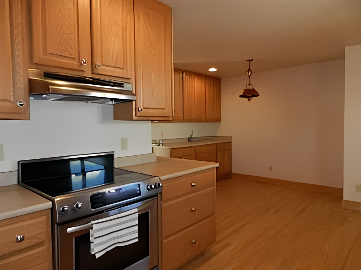 A modern kitchen with wooden cabinets, a stainless steel stove, and wood flooring.