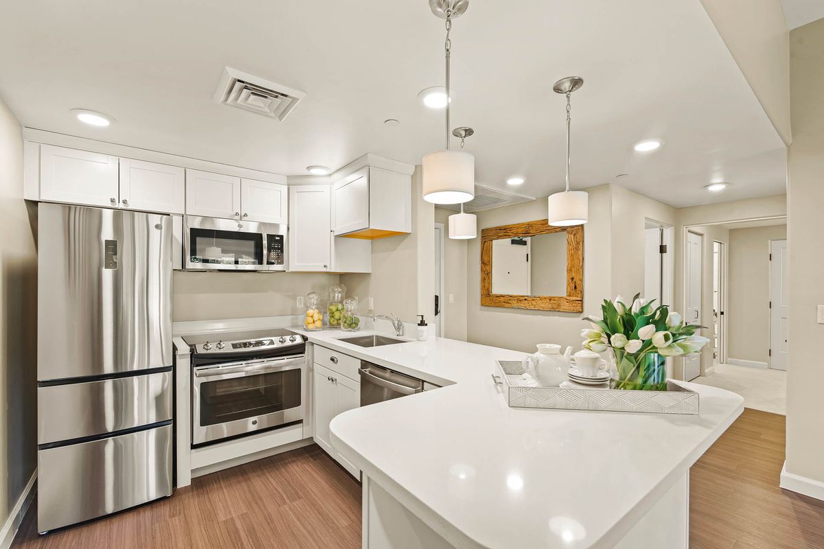A modern kitchen with white cabinets, stainless steel appliances, and elegant pendant lighting.