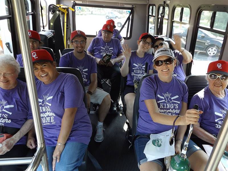 A group of people wearing matching purple t-shirts and hats sitting inside a bus, smiling at the camera.