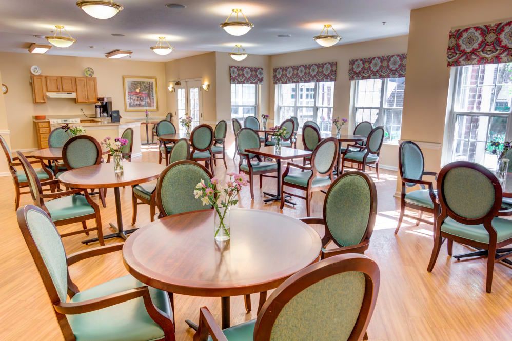 A well-lit dining area with multiple tables and chairs, adorned with small floral centerpieces.