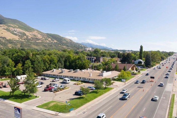 Aerial view of a residential area with buildings, a road with vehicles, and mountains in the background.
