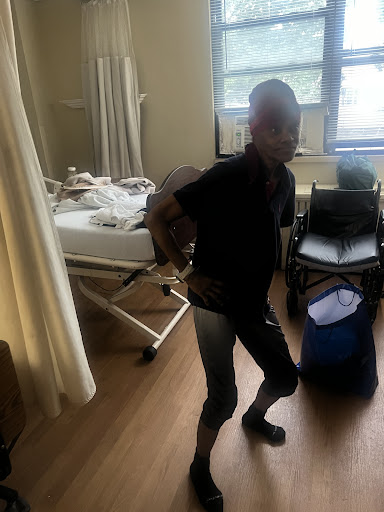 A person in a hospital room, standing near a bed and some medical equipment.