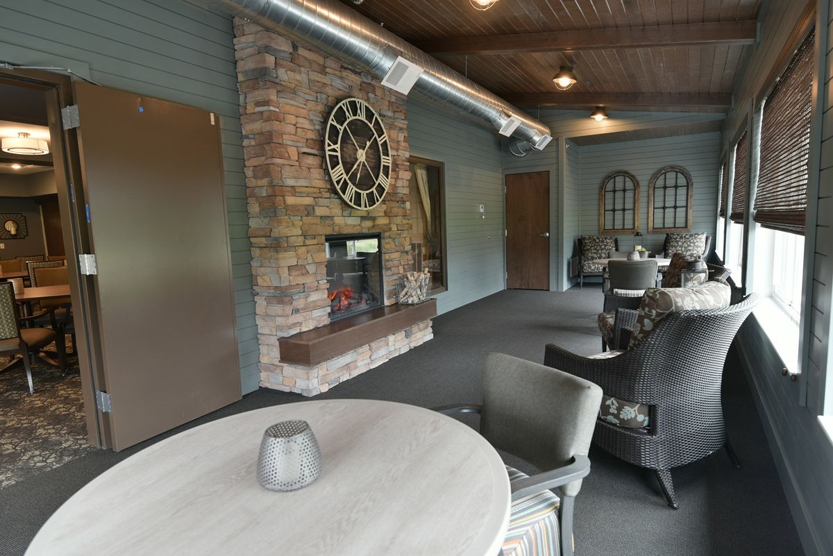 A cozy indoor seating area featuring a large clock above a fireplace, surrounded by tables and chairs.