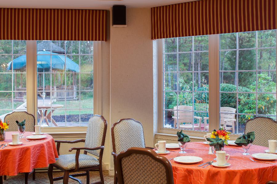 A cozy dining room with tables set for a meal, featuring large windows that provide a view of the outdoor patio.