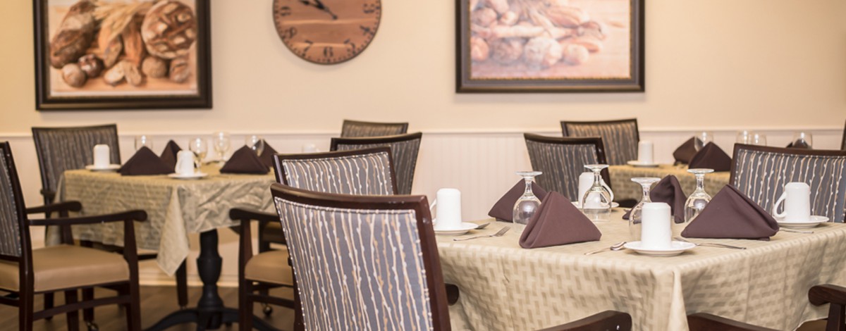 A cozy dining area with neatly arranged tables and chairs, featuring a wall clock and artwork.